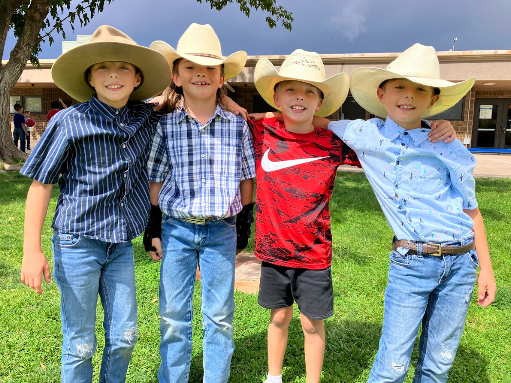 Four boys with cowboy hats, standing outside in the grass 